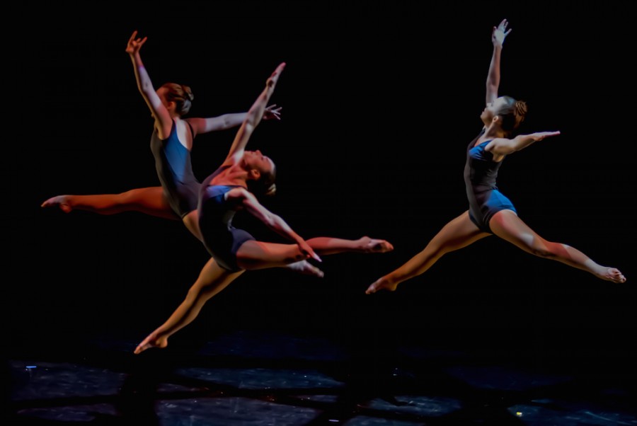 Dancers leap across the stage, performing a piece for the audience. 