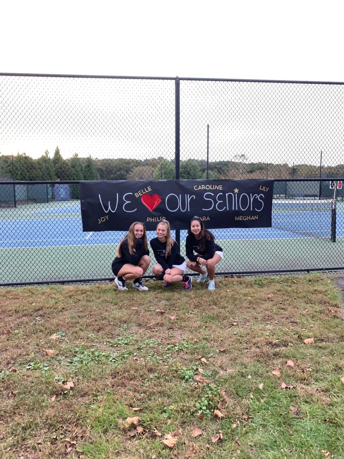 Seniors Caroline Dycio (left), Meghan Golden (middle), and Belle Ditthavong (right) pose in front of the poster team parents made honoring the seniors on the Girls' Varsity Tennis team.